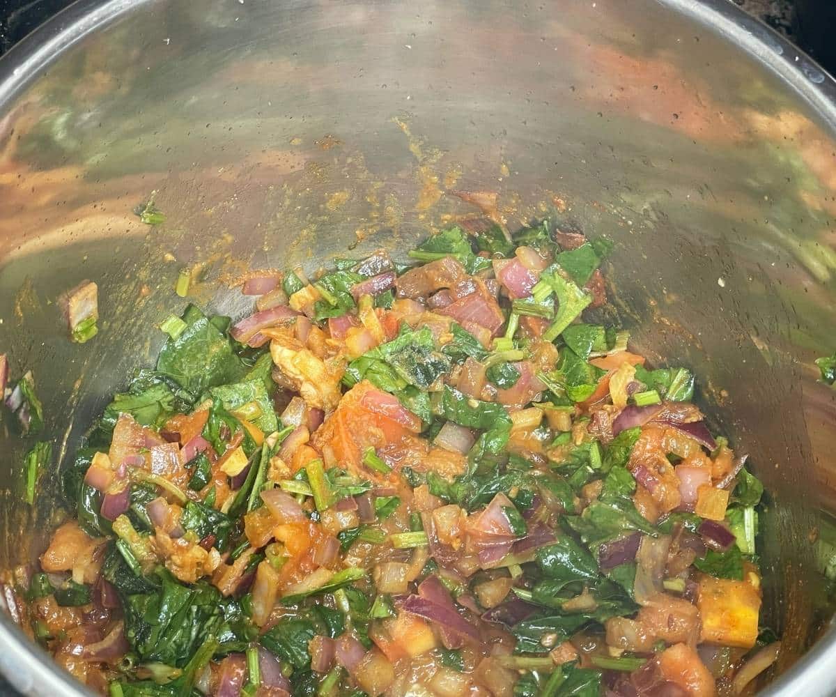 A pot is with spinach and tomatoes and spices for Curry.