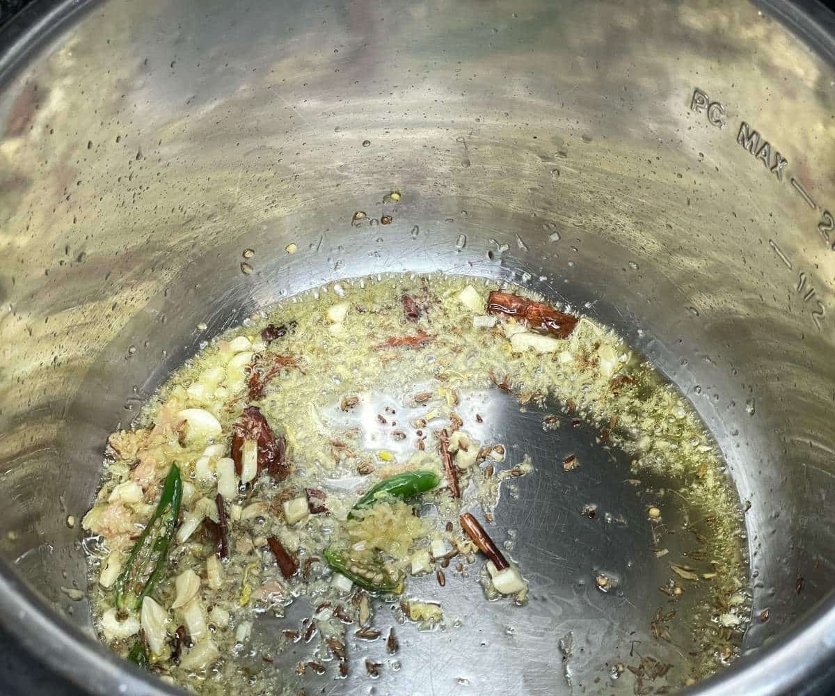 A pot is with spices, ginger, garlic and green chilies in cooking mode.