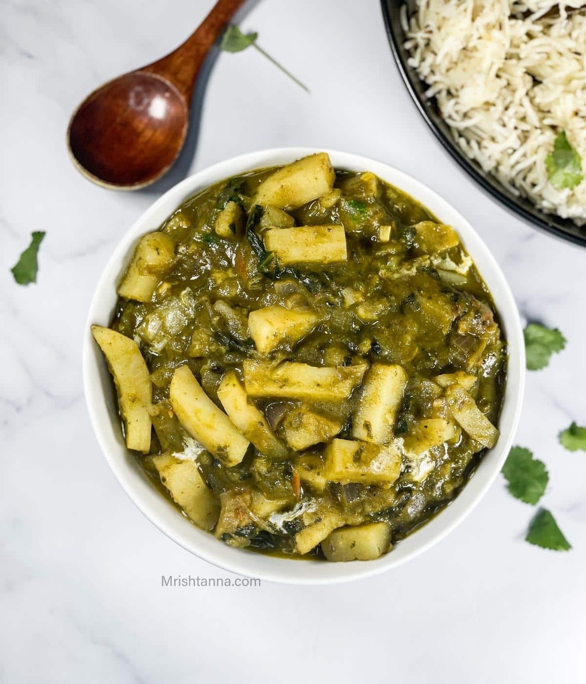 A bowl of aloo palak Curry is on the marble table.