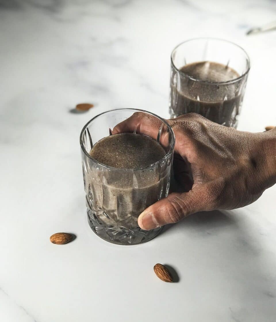 A man is holding the glass of ragi malt over the table