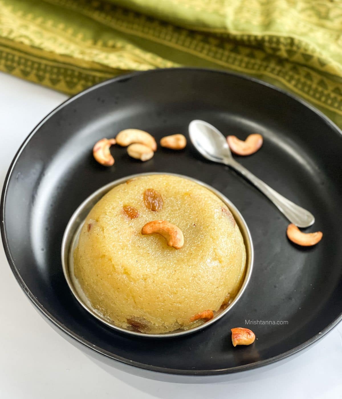 A bowl of rava kesari is on the plate with a spoon.