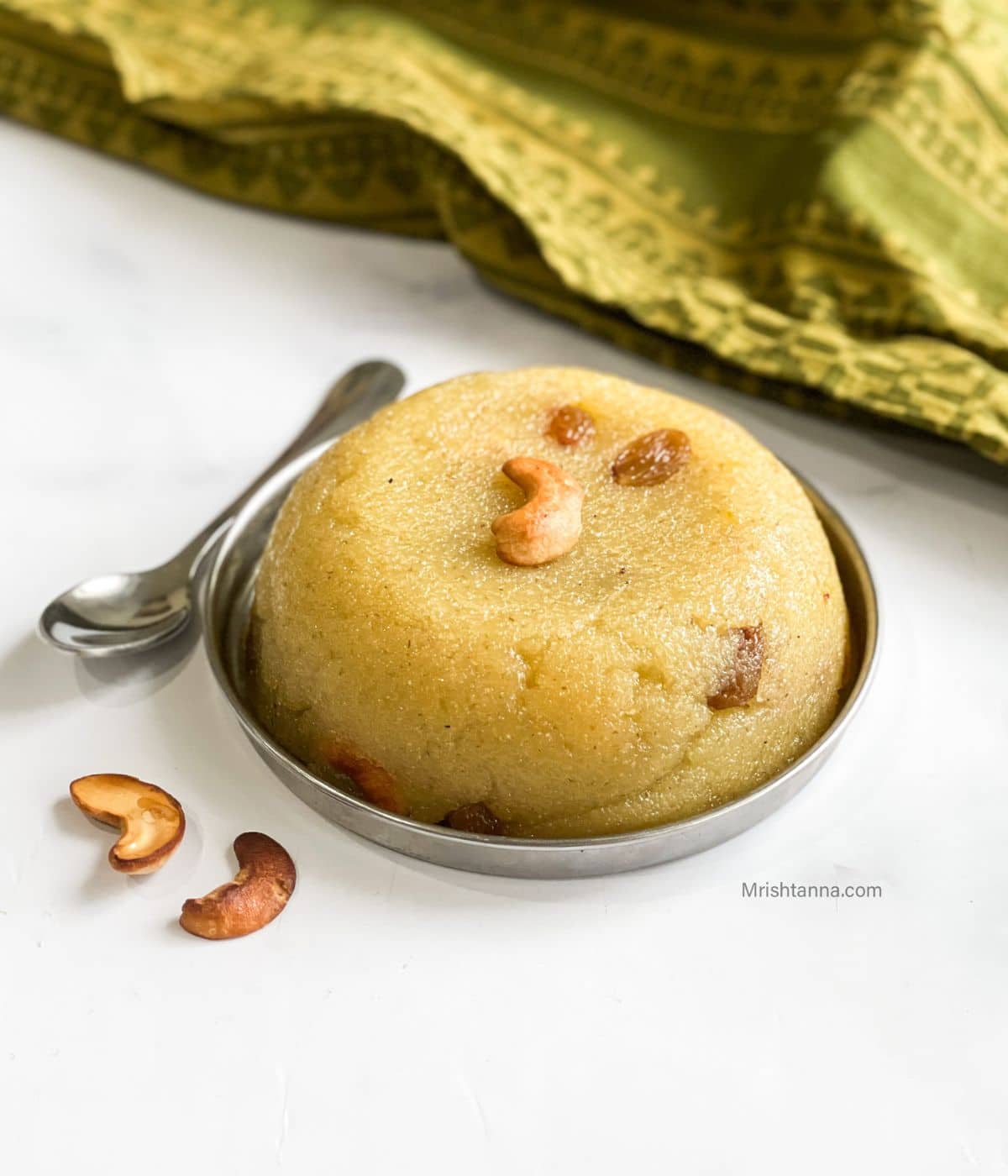 A plate of rava kesari is on the table with a spoon by the side.