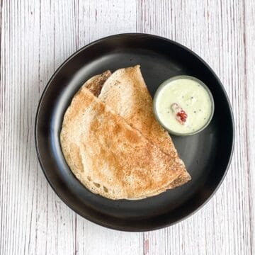A plate of wheat dosa is on the table with chutney.