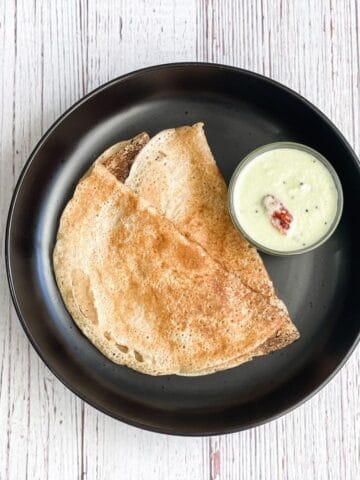 A plate of wheat dosa is on the table with chutney.