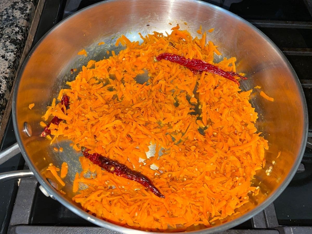 A pan is with grated carrots over the heat