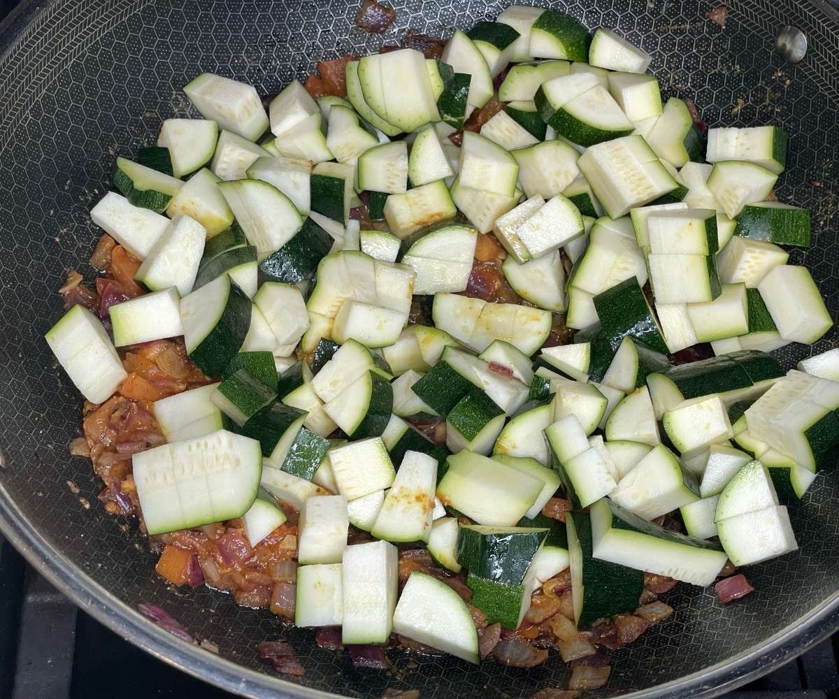 A close-up of a frying pan filled with zucchini and chickpeas for the curry.