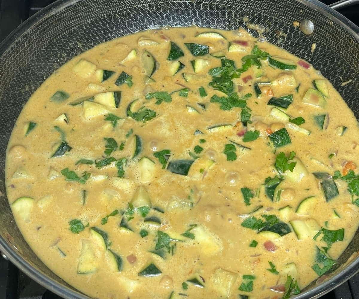 A large skillet filled with creamy zucchini curry simmers on the stove.