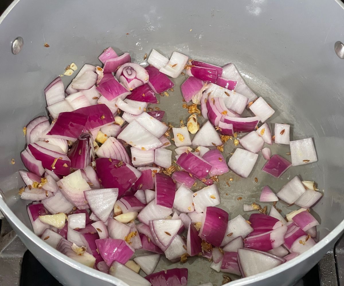 A pan is with spices and onions over the heat.