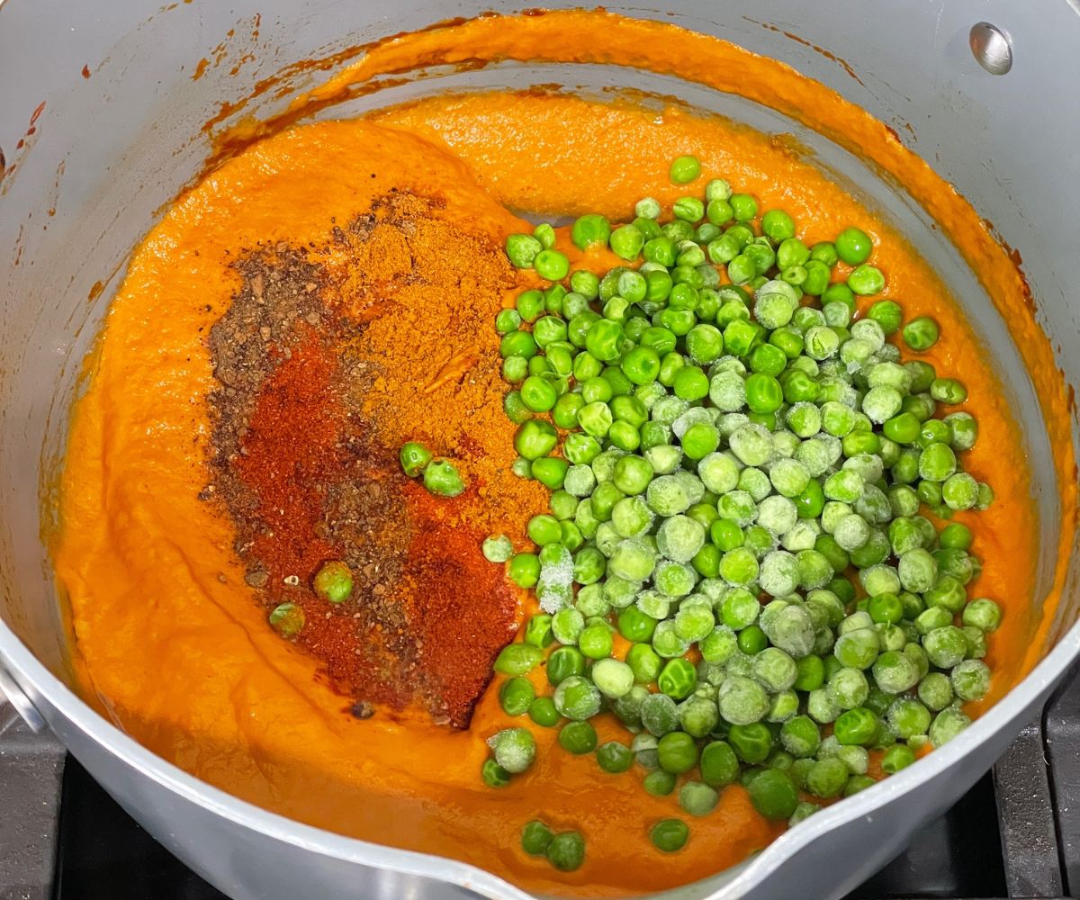 A pot is with blended masala,spices, and green peas over the stove top.