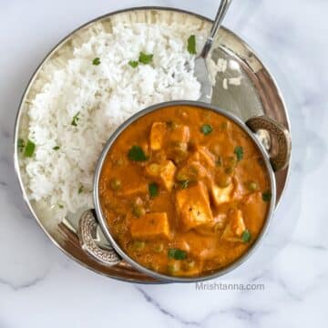 A bowl of tofu matar is on the plate with rice and spoon.