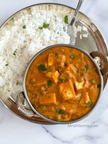 A bowl of tofu matar is on the plate with rice and spoon.