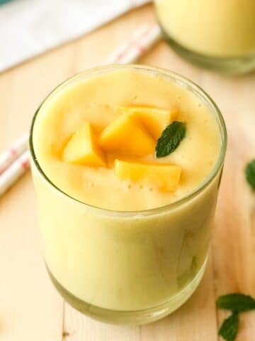 a glass is filled with mango lassi and topped with mango cubes and mint leaves