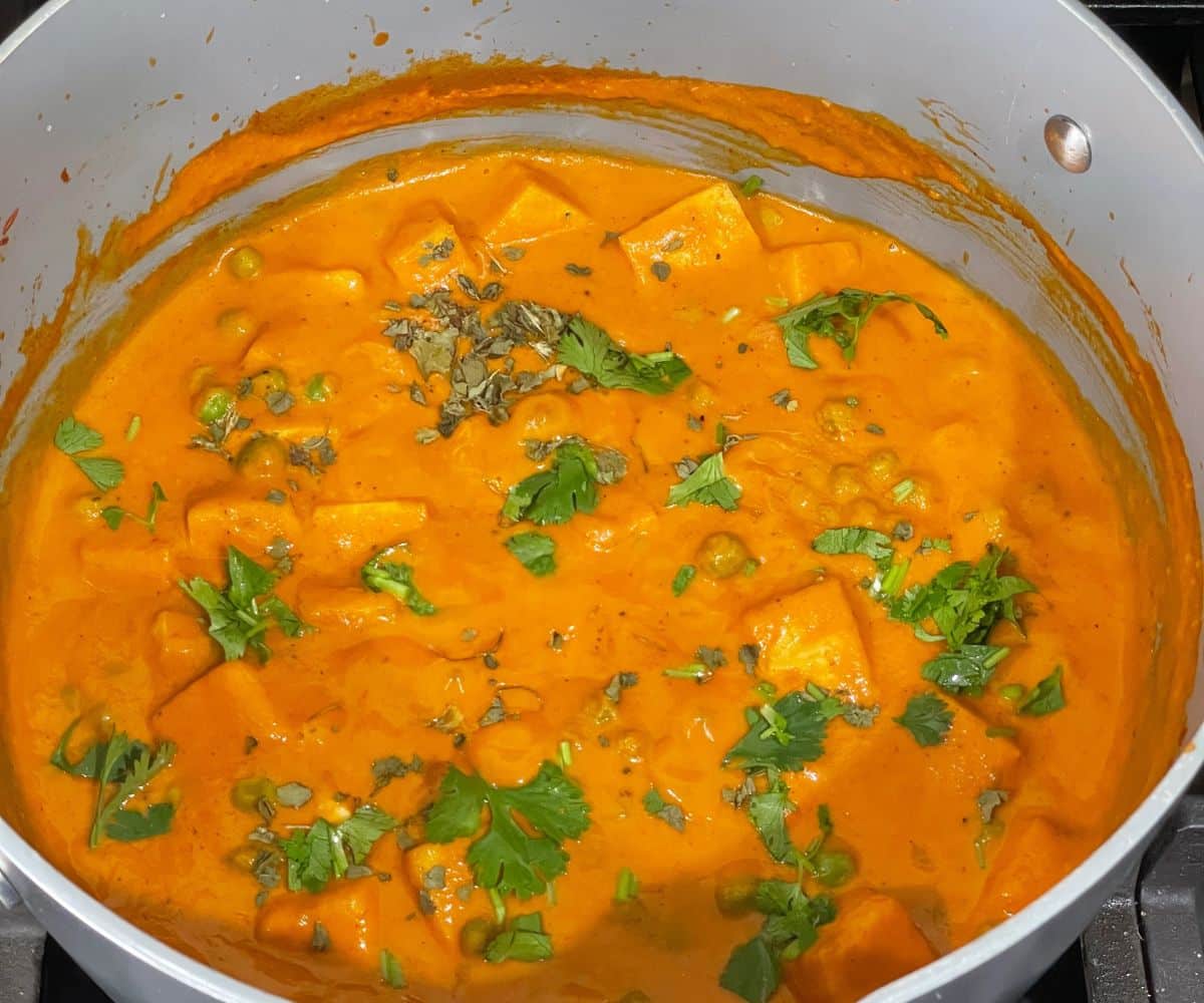 A pot of vegan matar paneer is on the stove top.