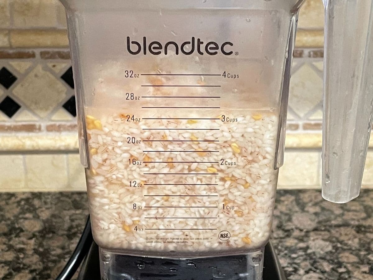 A blender is filled with soaked rice and methi seeds and water