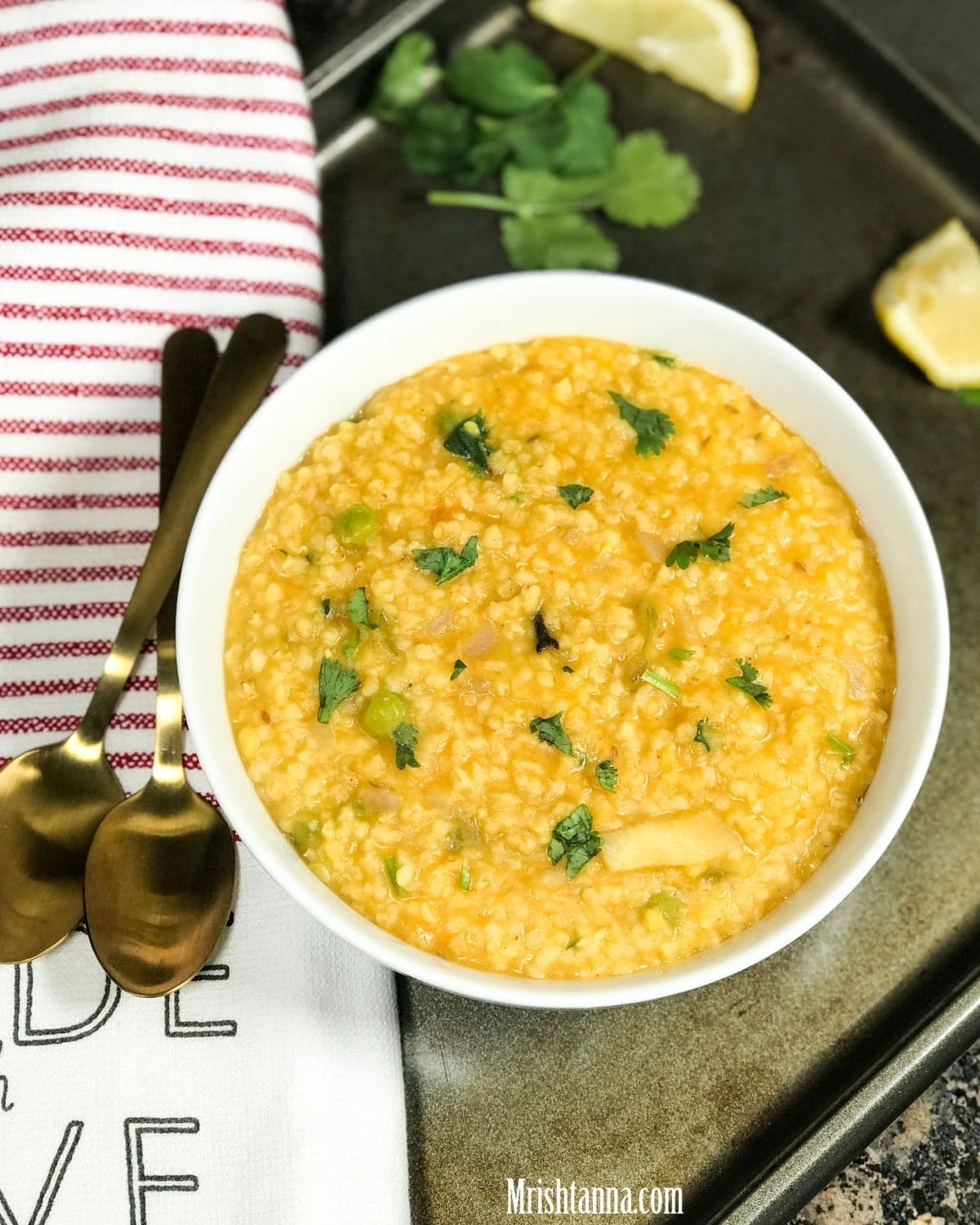 A white bowl with dalia khicdi and garnished with cilantro and lemon slices