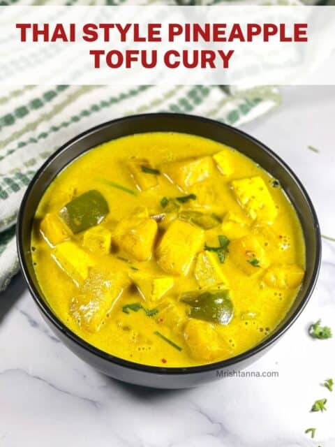 A black bowl is filled with Thai pineapple curry.