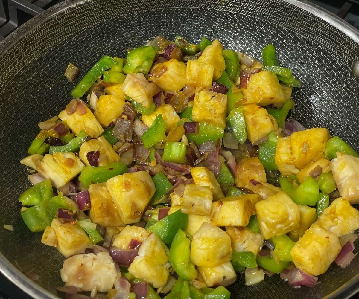 A pan is with pineapple tofu curry ingredients over the stove.