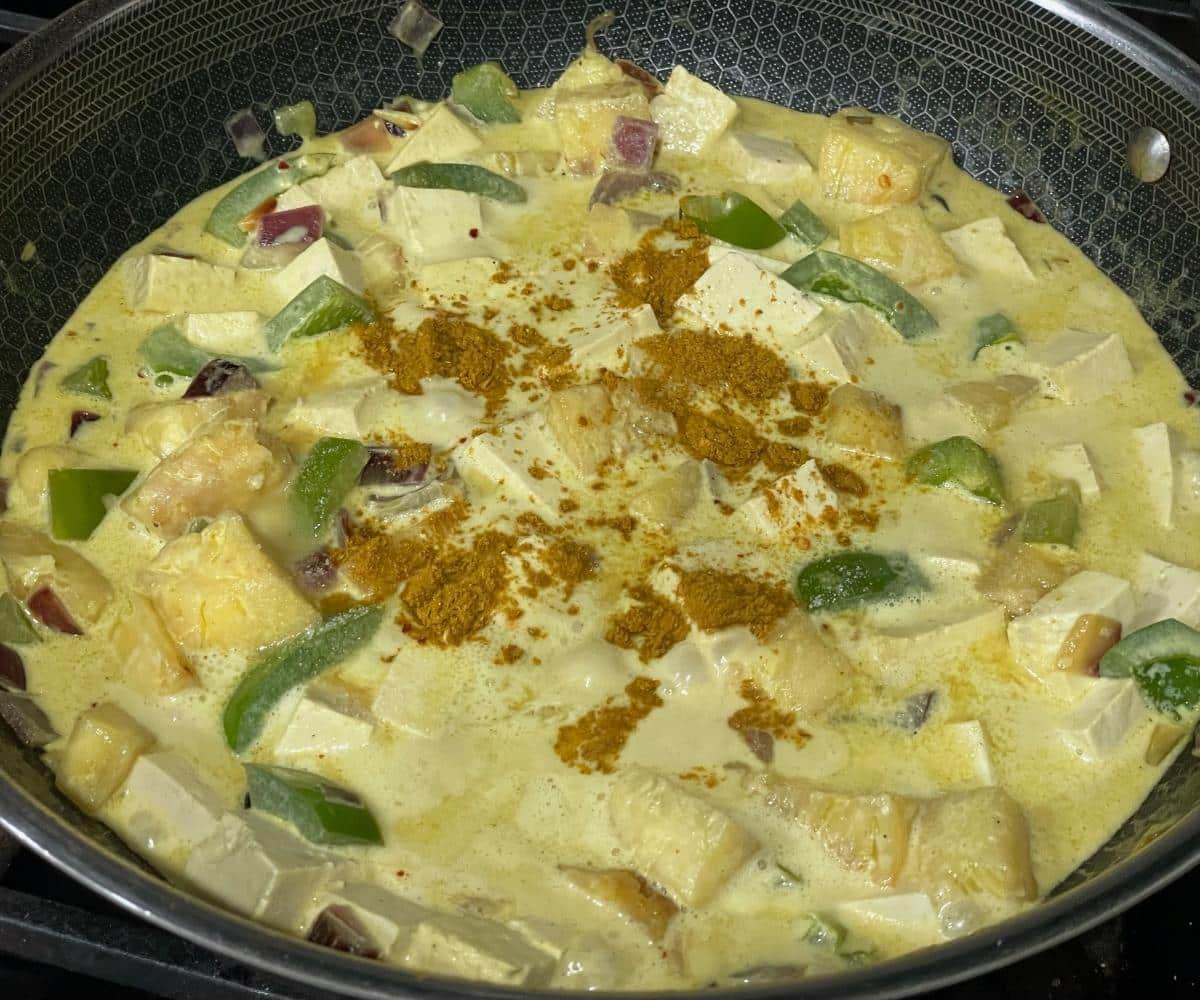 A pan contains pineapple, tofu and coconut milk over the heat.