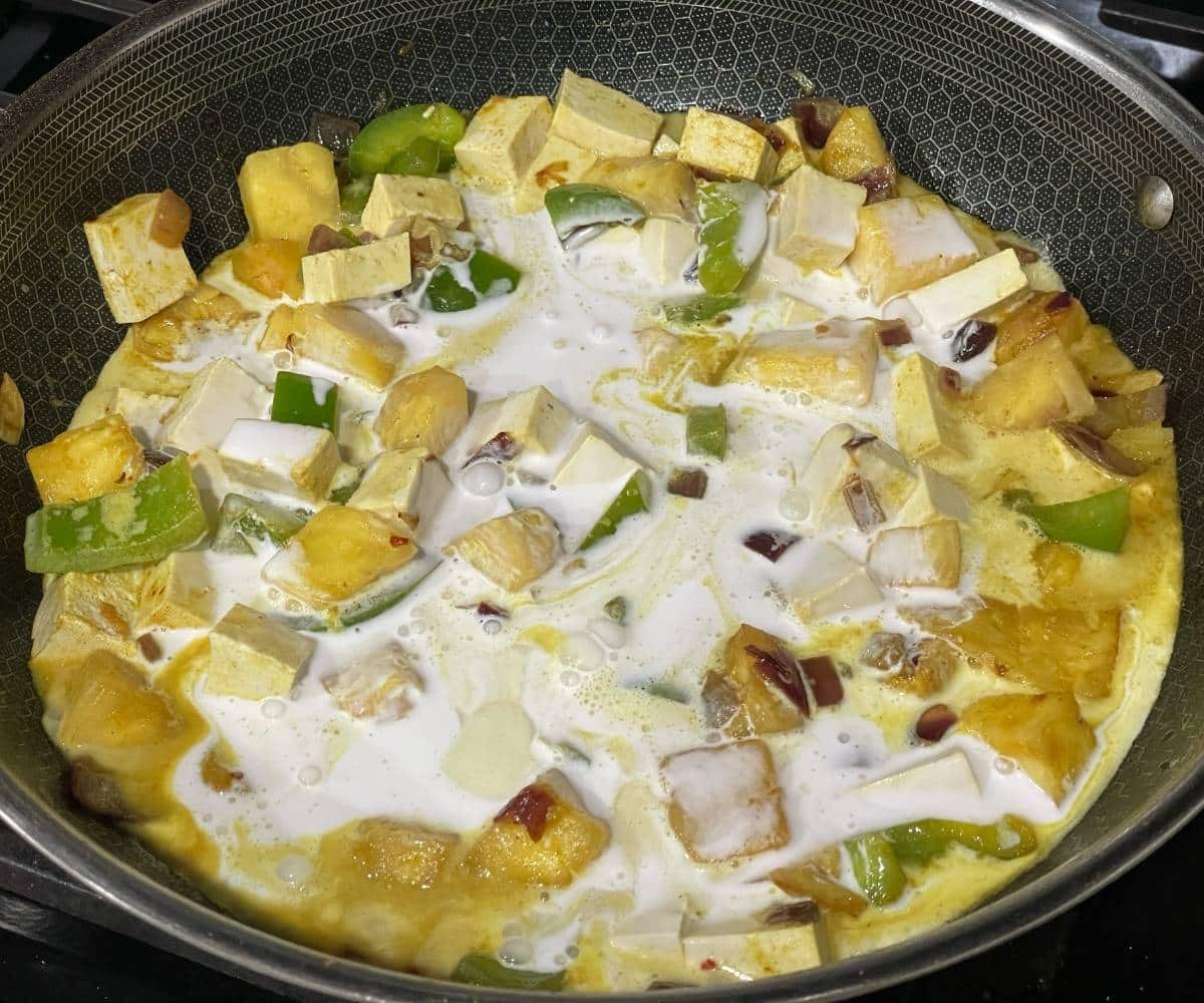 A pan contains pineapple, tofu and coconut milk over the heat.