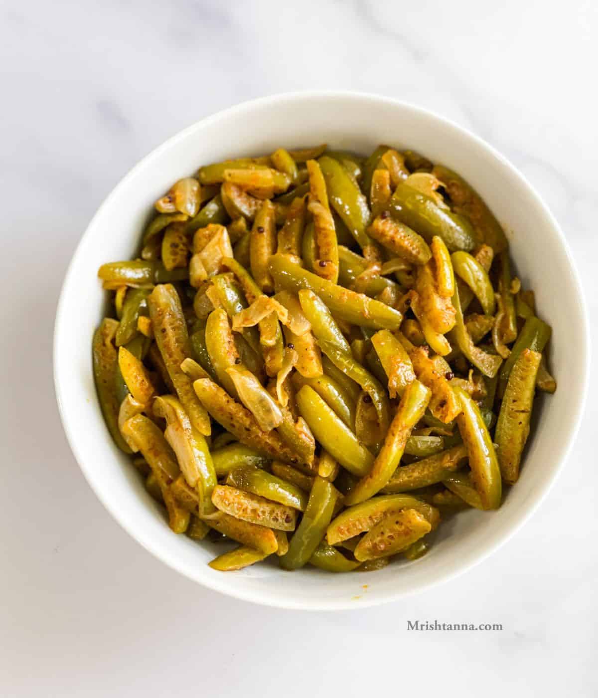 A bowl of tindora fry is on the white marble table.