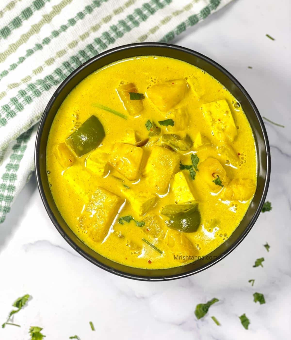 Thai style pineapple tofu curry made with coconut milk, tofu cubes, pineapple chunks, and bell peppers served in a black bowl.