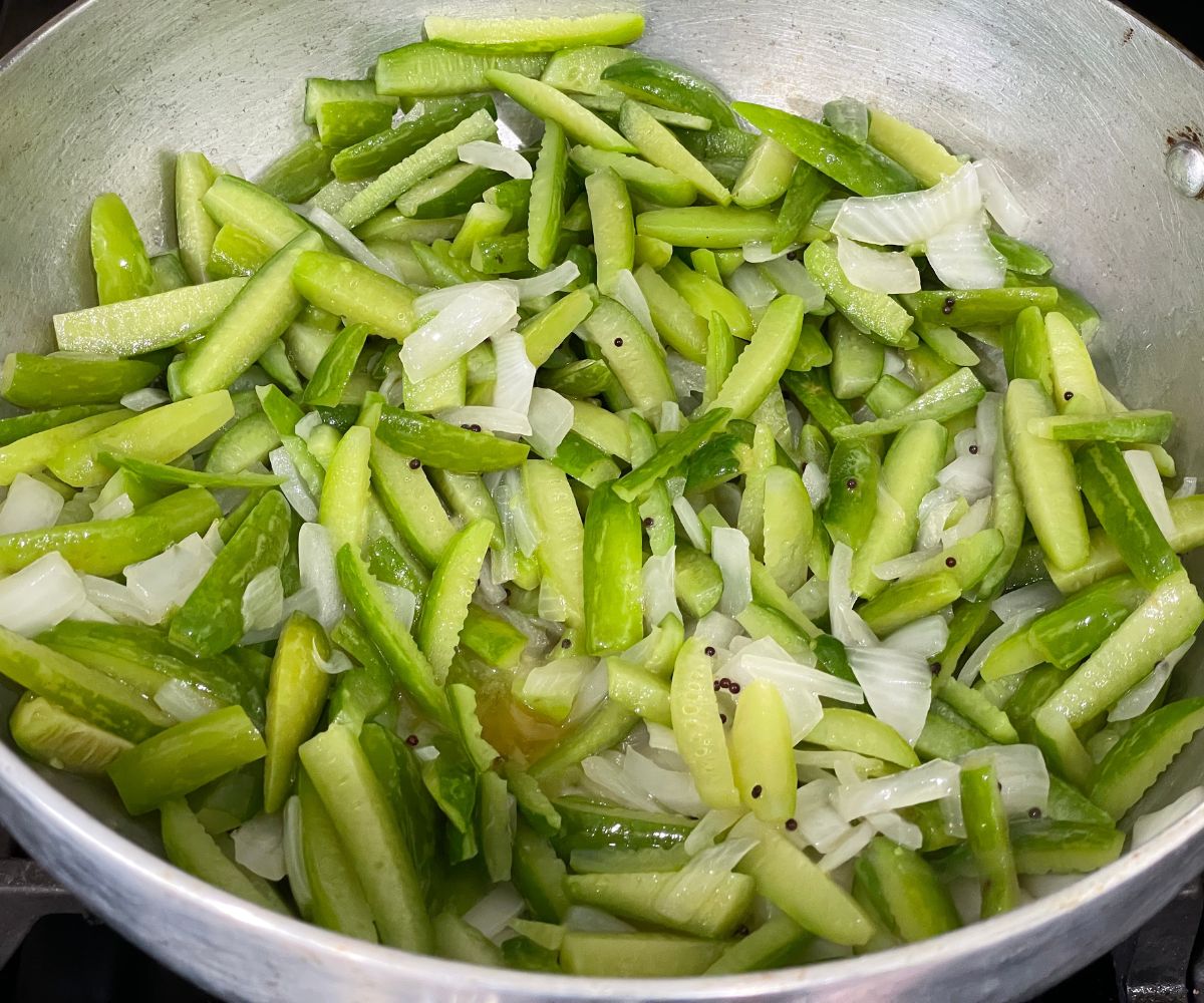 A pan is with onions and tindora over the stove top.