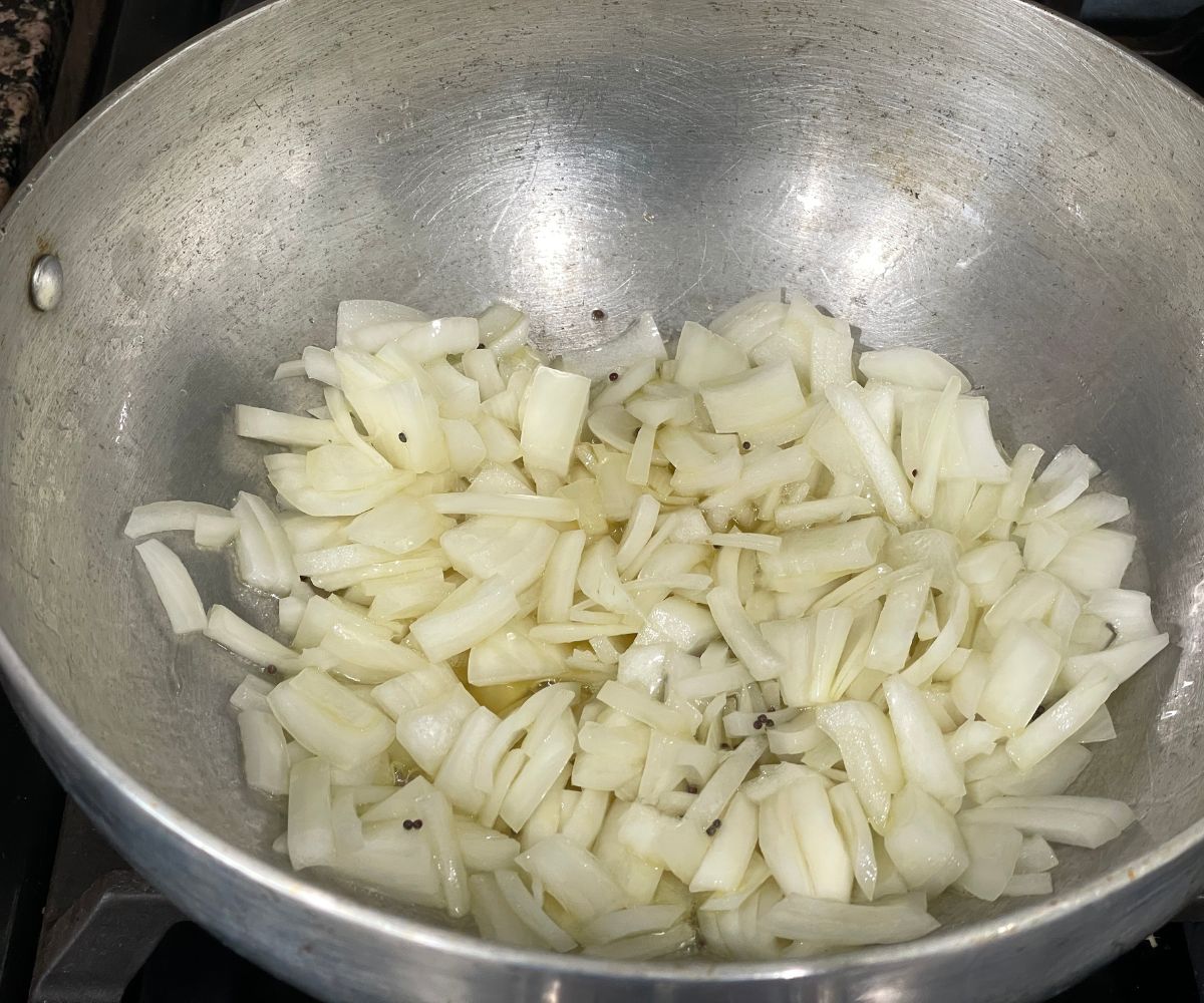 A kadai is with oil, and chopped onions over the heat.