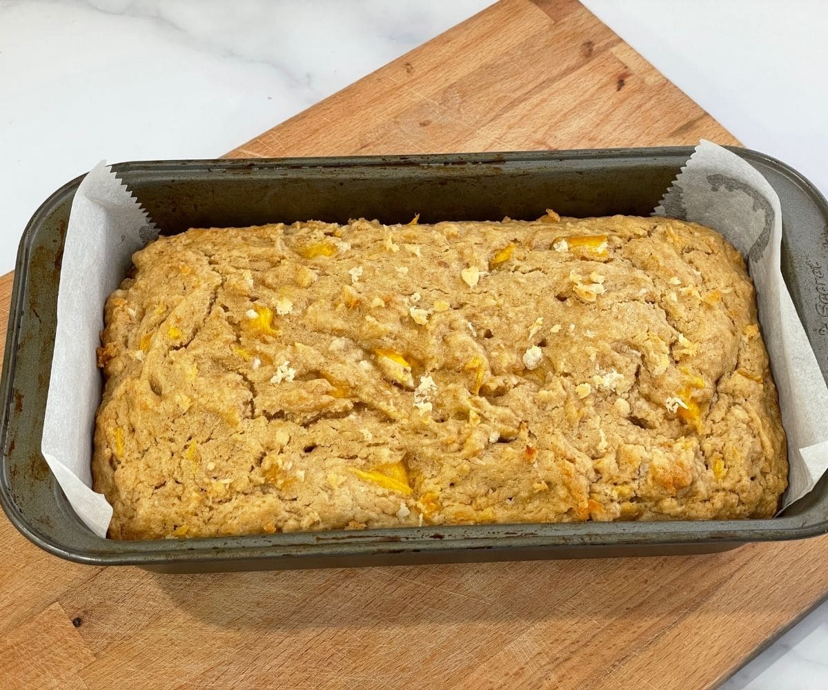 A pan of mango bread is on the wooden board.