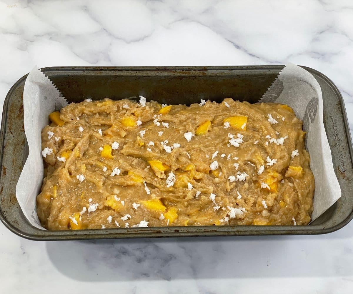 A loaf pan is with mango bread batter.