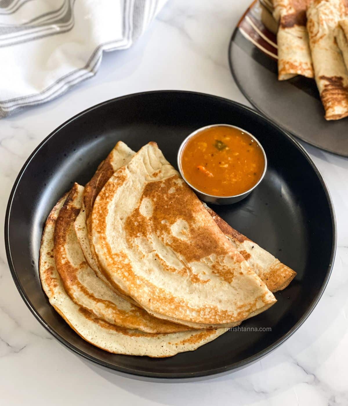 Three quinoa dosa and bowl of sambar is on the plate.