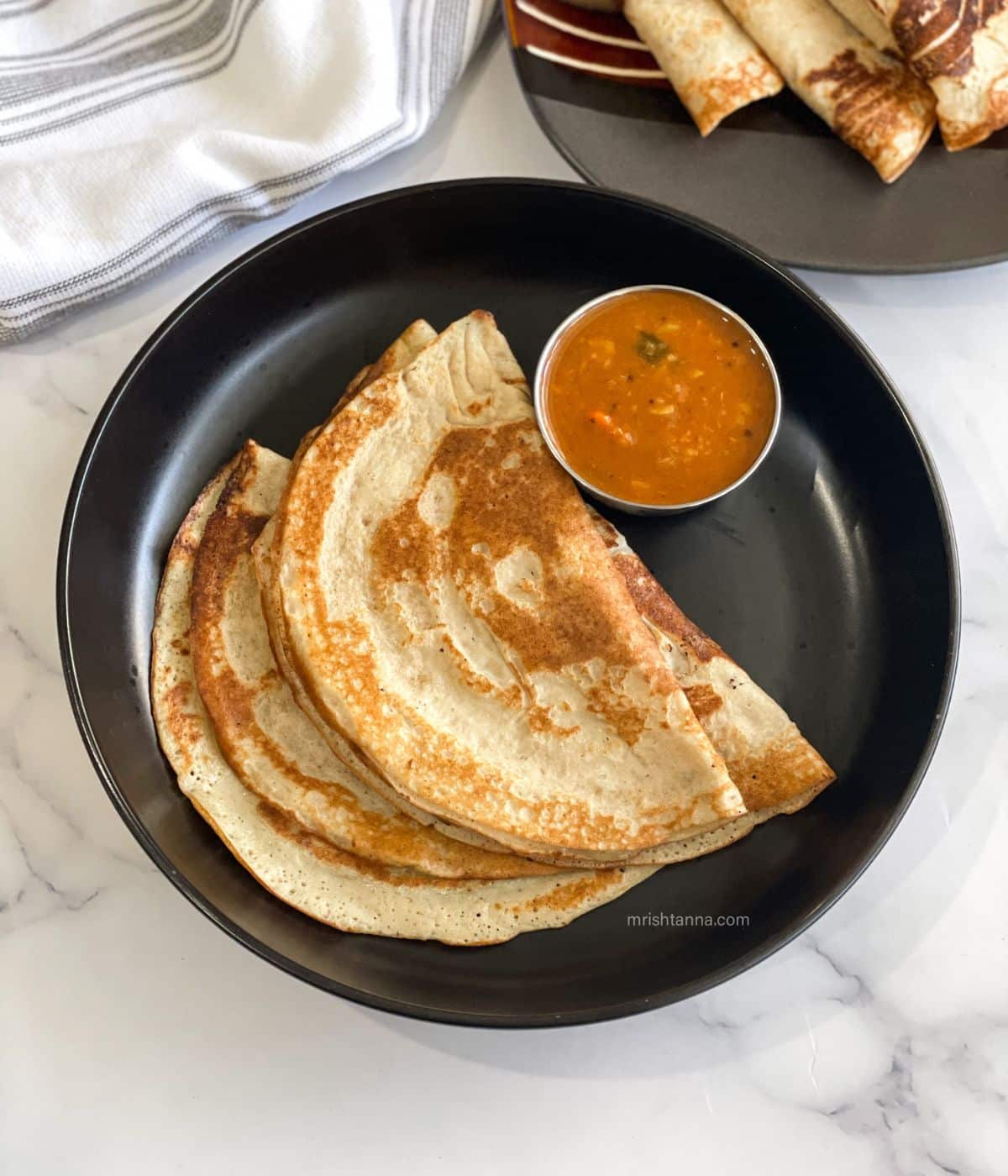 A plate has three quinoa dosa and a bowl of sambar.