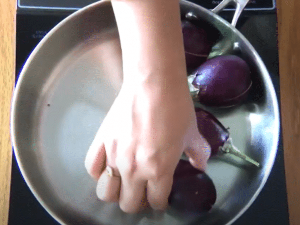 A person placing them eggplant in a bowl, with Onion and Coconut