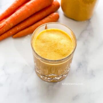 A glass of carrot milkshake is on the marble table