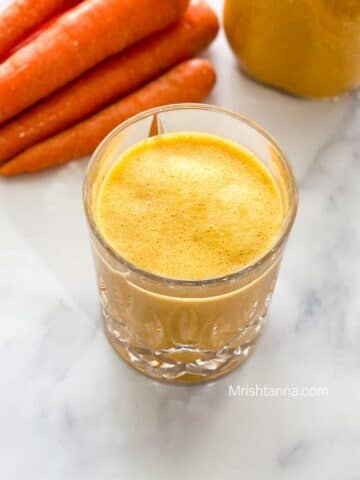 A glass of carrot milkshake is on the marble table