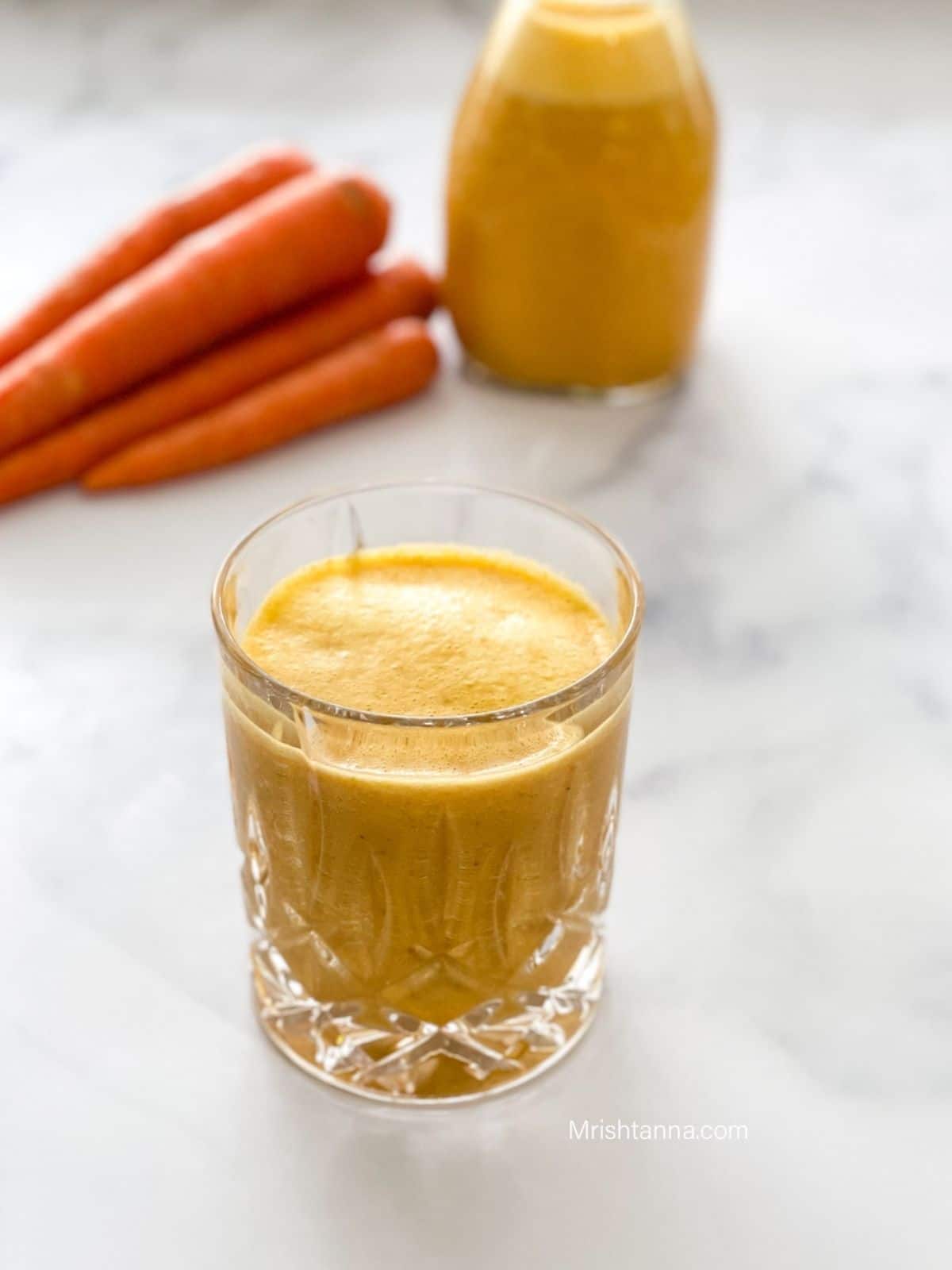 A glass of carrot milkshake is on the table