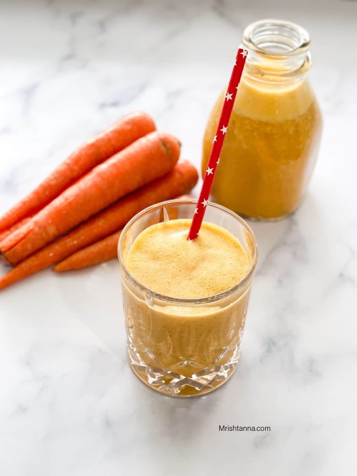 A glass is filled with carrot milkshake and a straw is inserted inside the glass
