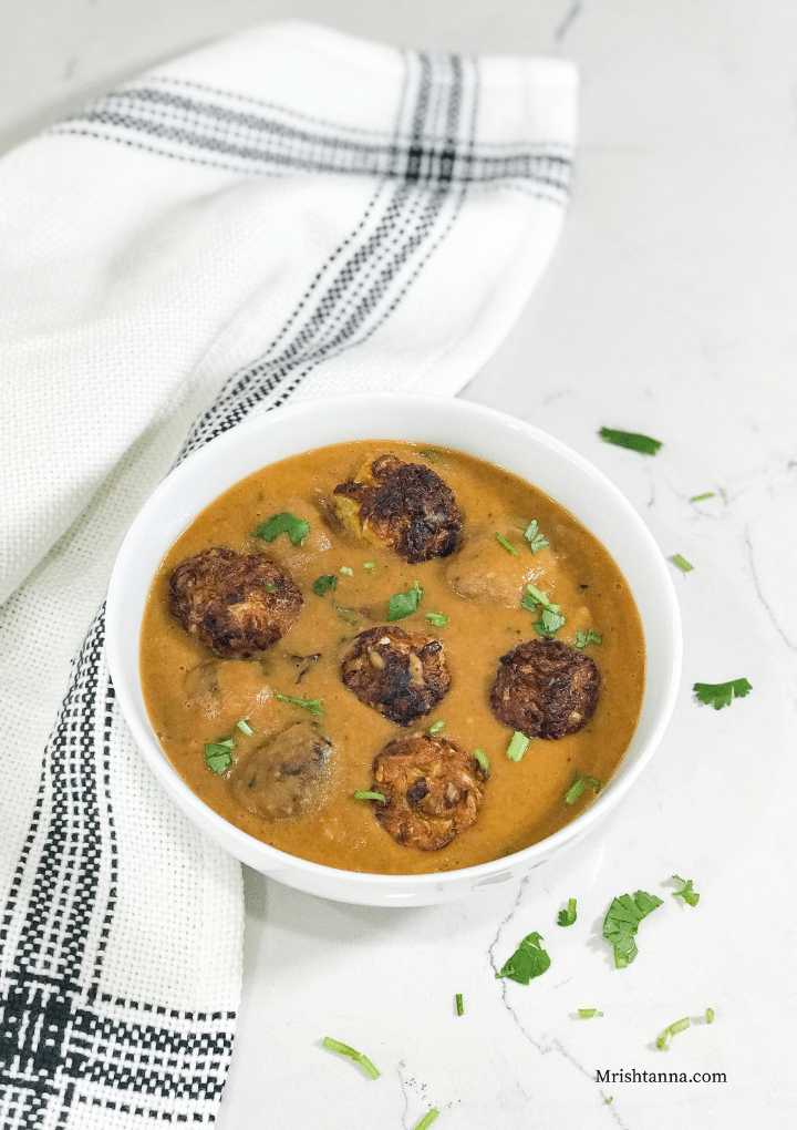 A white bowl filled with gravy and cabbage kofta