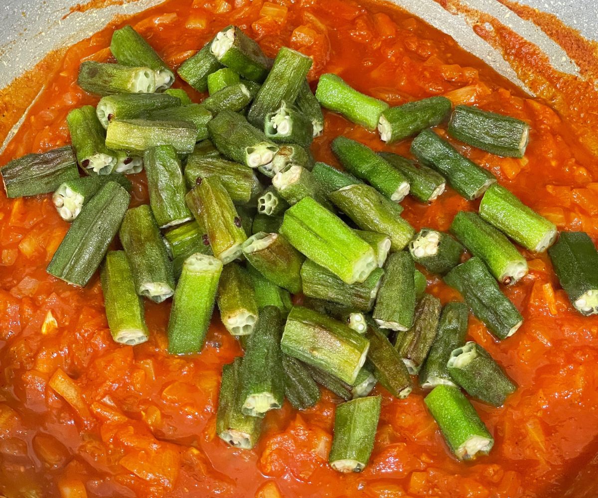A pan is with fried okra and masala over the heat.