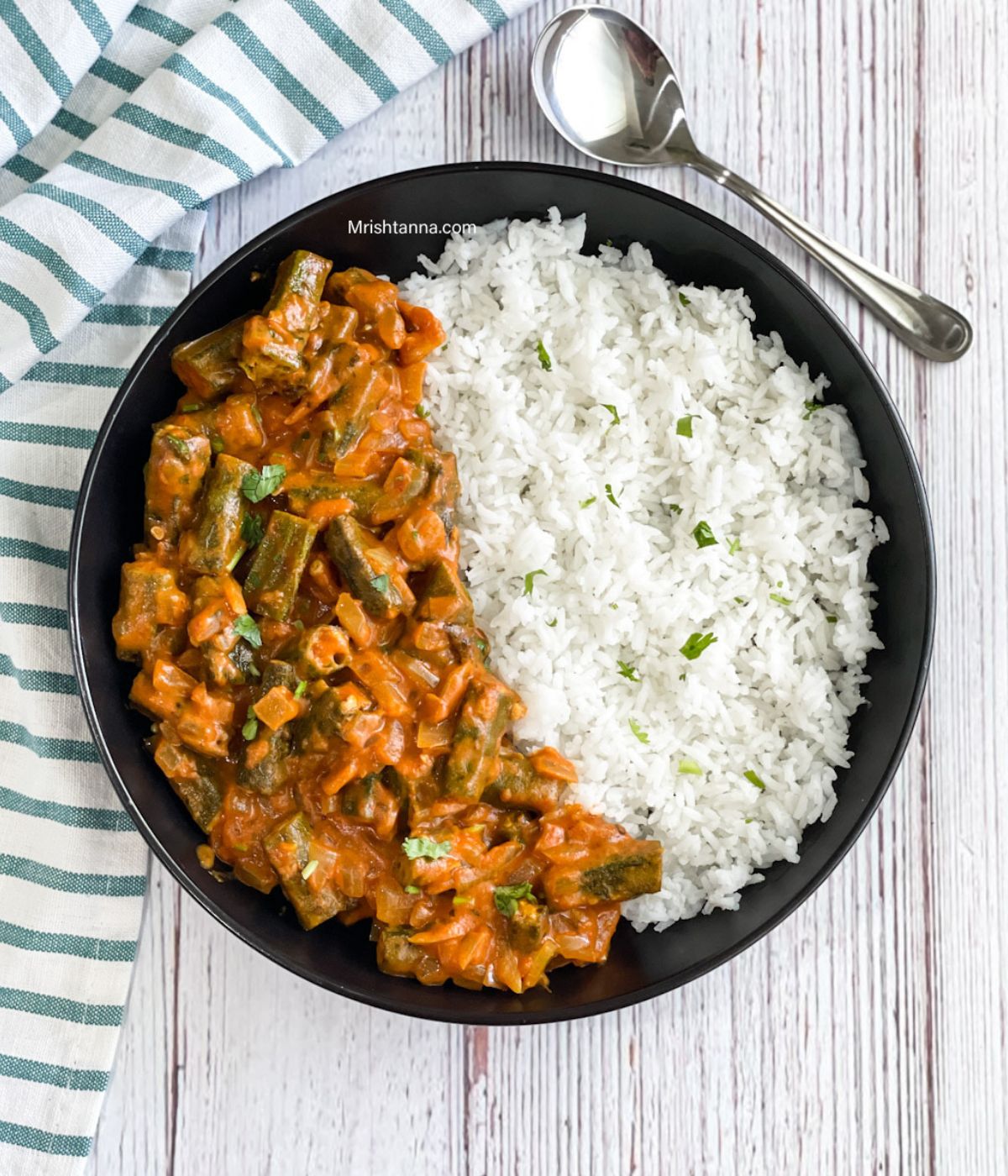 The head shot of the plate is with okra masala and rice with a spoon by the side.