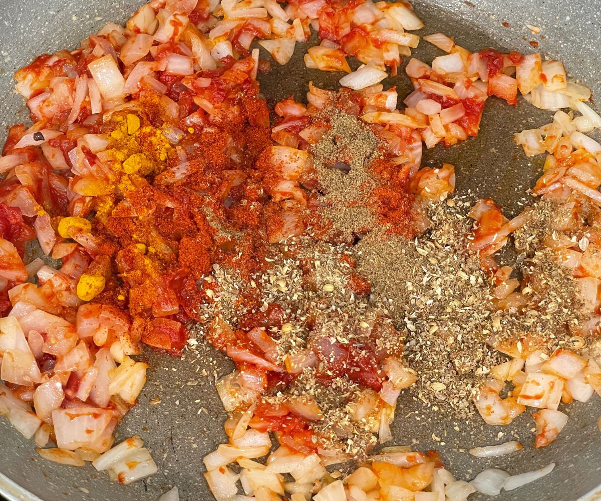 A large pan is with spices and onion tomato paste.