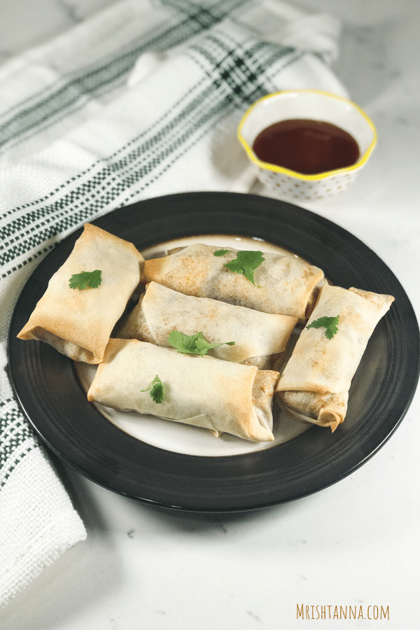 A plate of Baked Spring Rolls is on the table with sauce on the side