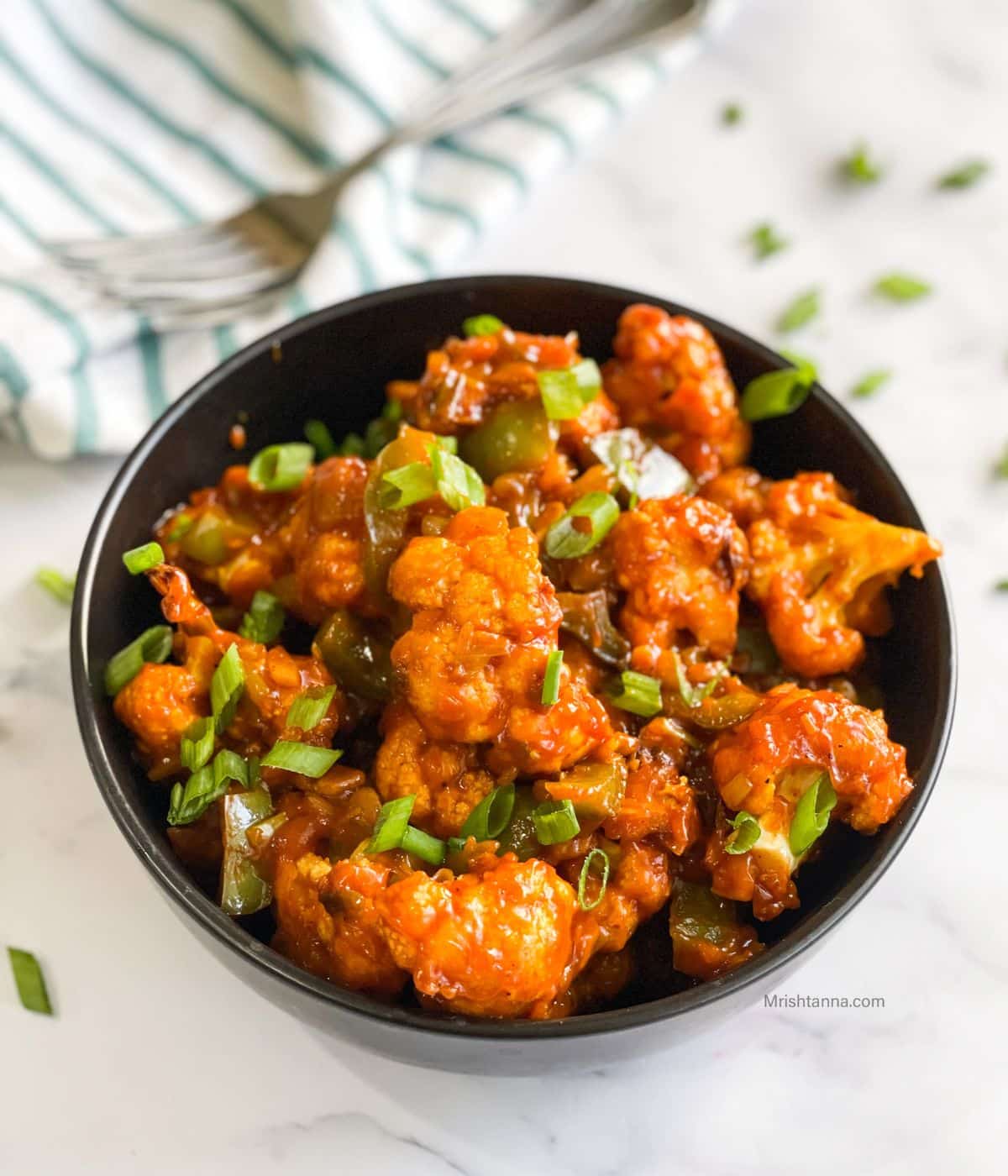 Gobi Manchurian is on the bowl topped with green onions.