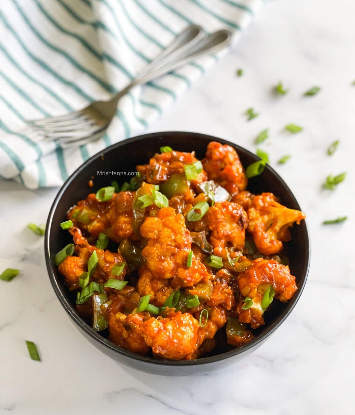 A bowl of air fried gobi manchurian is on the table with forks by the side.