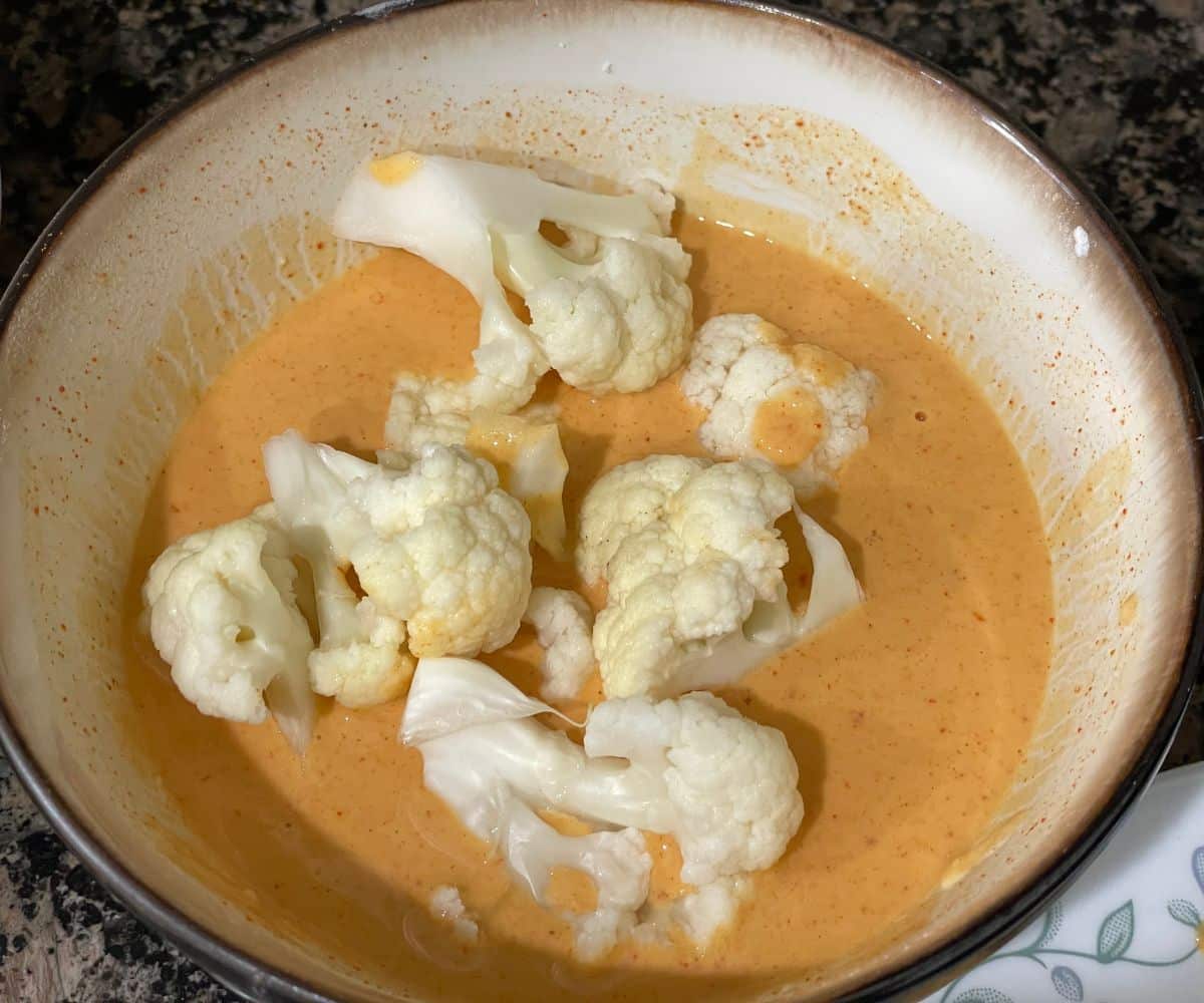 A bowl is with flour batter and cauliflower dipped into them.