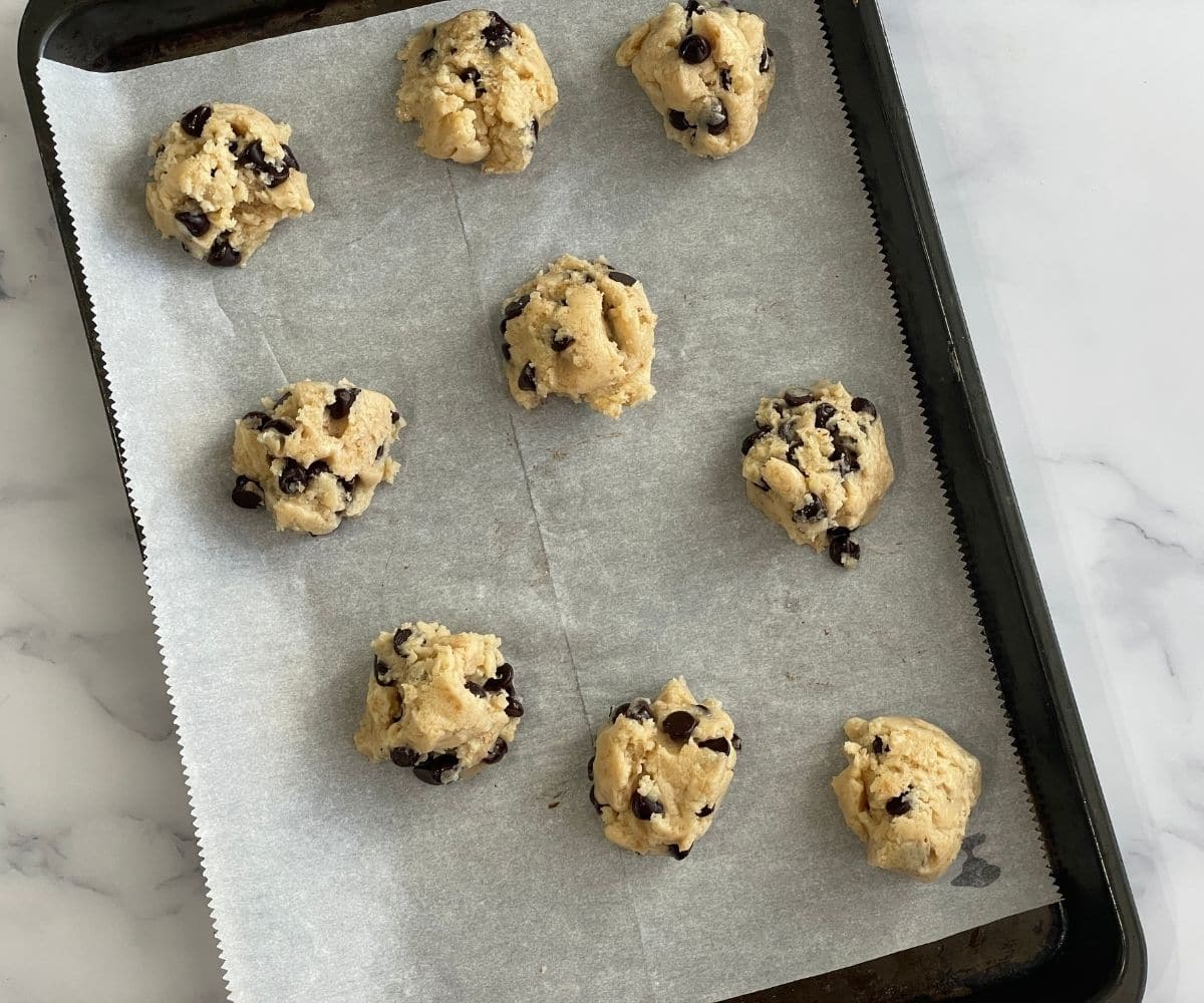 A baking tray is with raw cookie balls.