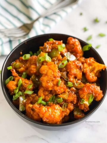 Gobi Manchurian is on the bowl topped with green onions.