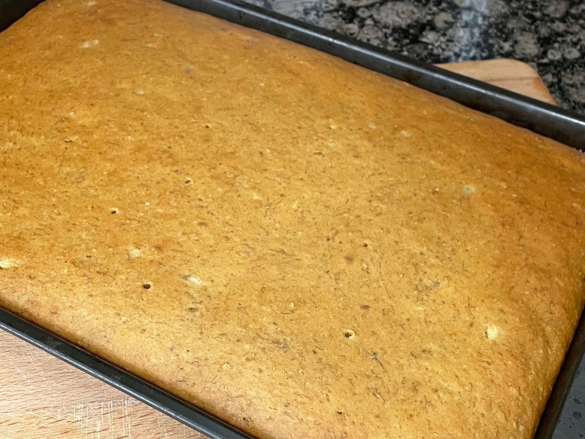 A sheet pan is with baked banana cake on the counter top.