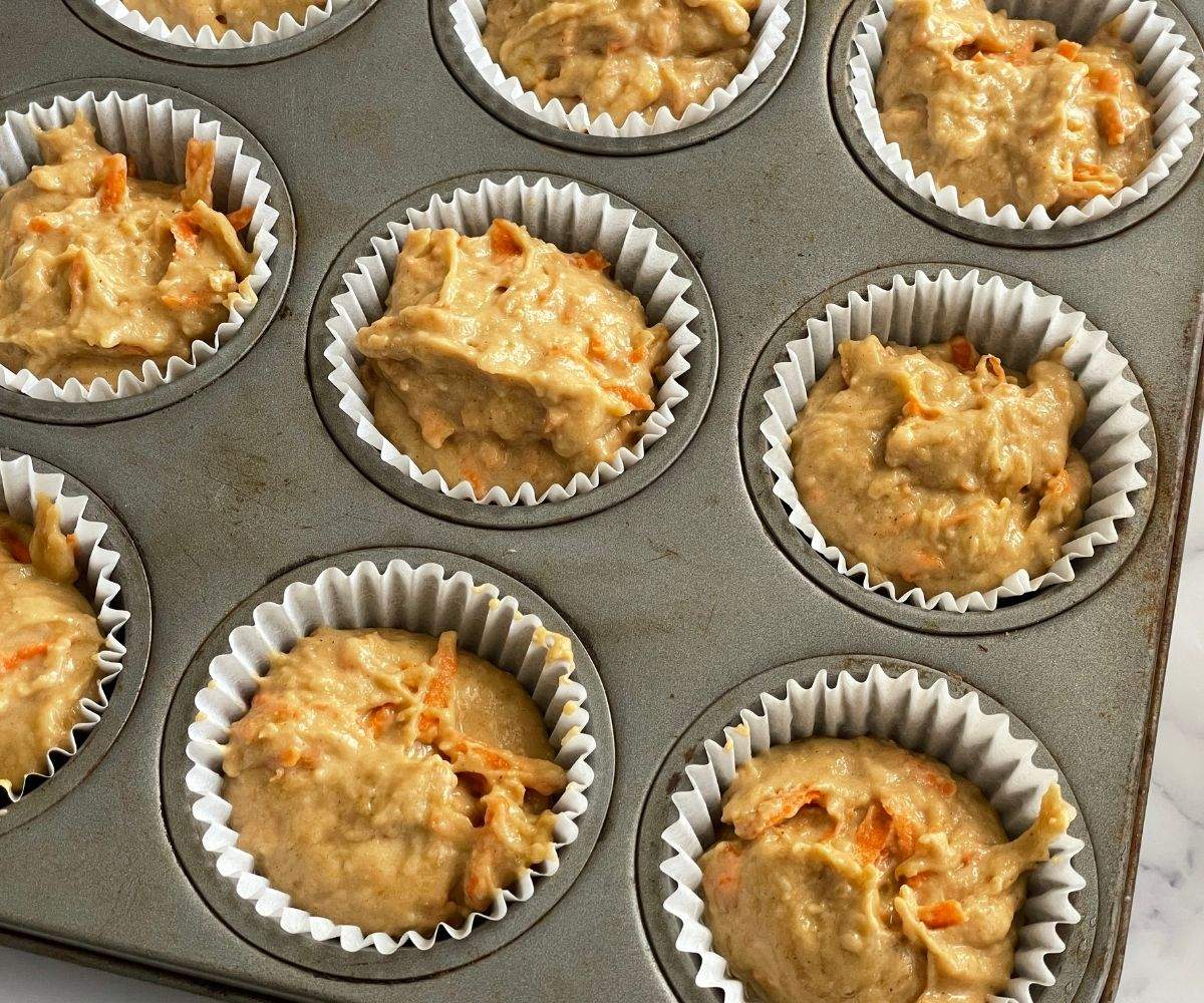 A muffin tray is filled with banana carrot muffin batter.