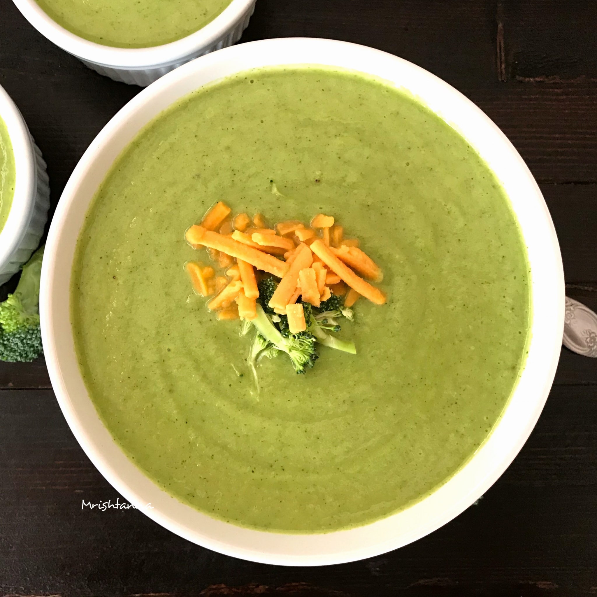 A bowl of Broccoli Soup is on the table topped with cheese