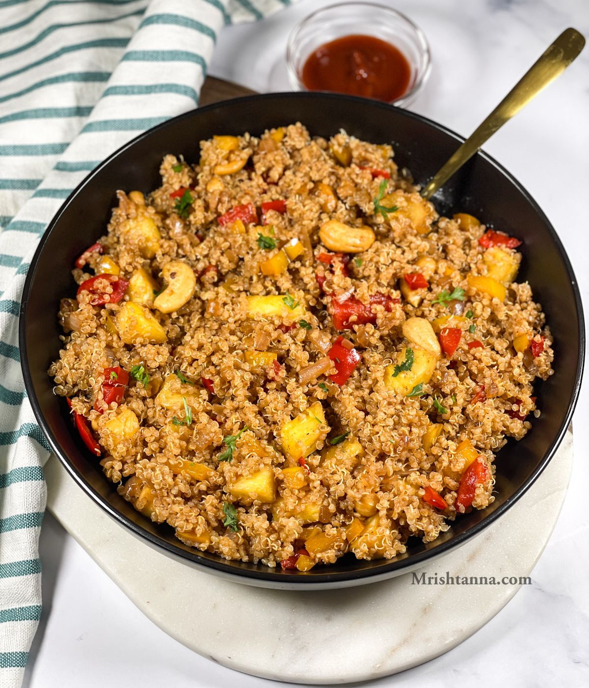 A plate of pineapple quinoa is on the table with golden spoon inserted.